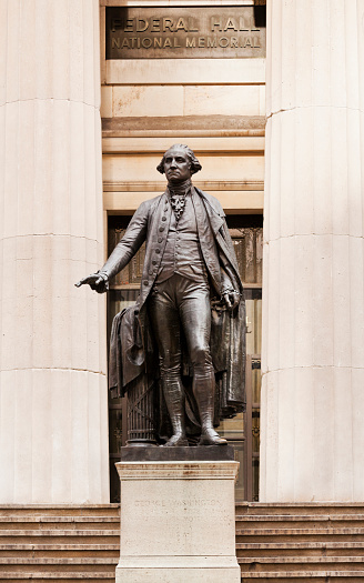 George Washington statue in front of the Federal Hall National Memorial in Wall Street in New York. This building was created in 1842 as the New York Customs House. Now it operates as a museum. The large bronze statue was created in 1883 by John Quincy Adams Ward and depicts him raising his hand from the Bible.