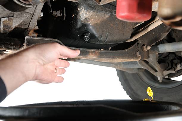 Reaching for engine oil drain plug "Hand reaching for engine oil drain plug under car, horizontal with copy space." stopper stock pictures, royalty-free photos & images