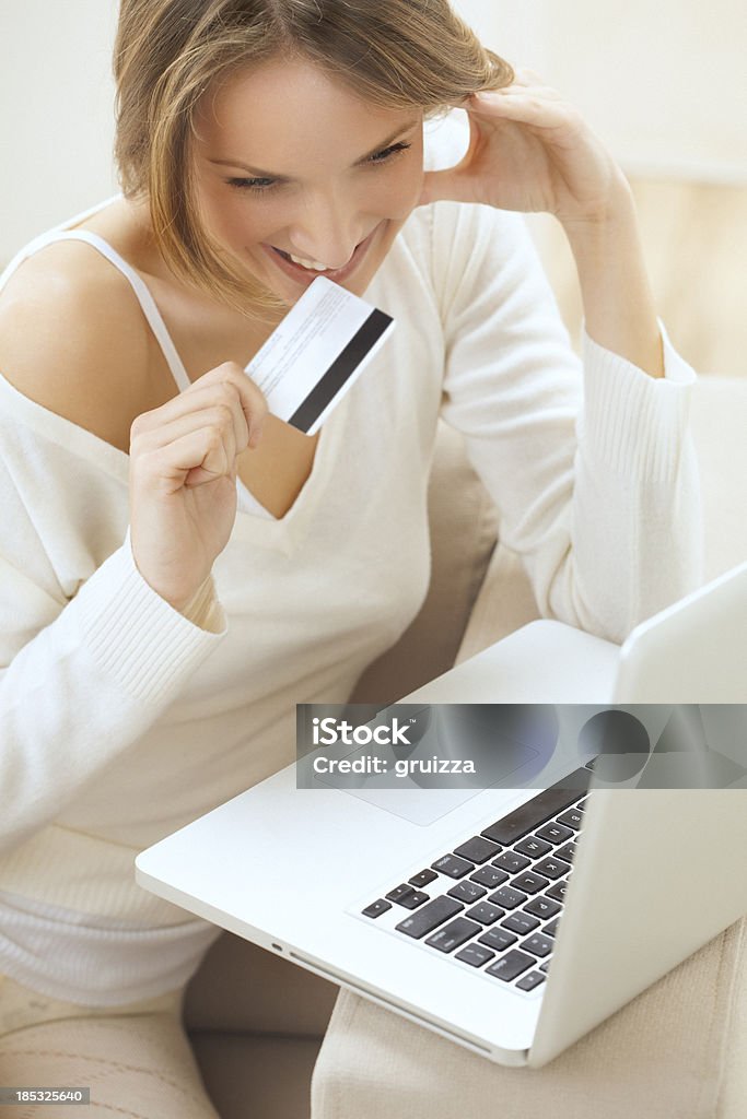 Beautiful smiling blond woman, shopping online from home "High key portrait of a cheerful, smiling, young, beautiful, blonde woman holding credit card on her lips, while using laptop in a brightly lit, modern living room. Shallow DOF. Developed from RAW; retouched with special care and attention; Small amount of grain added for best final impression. Adobe RGB color profile." Adult Stock Photo