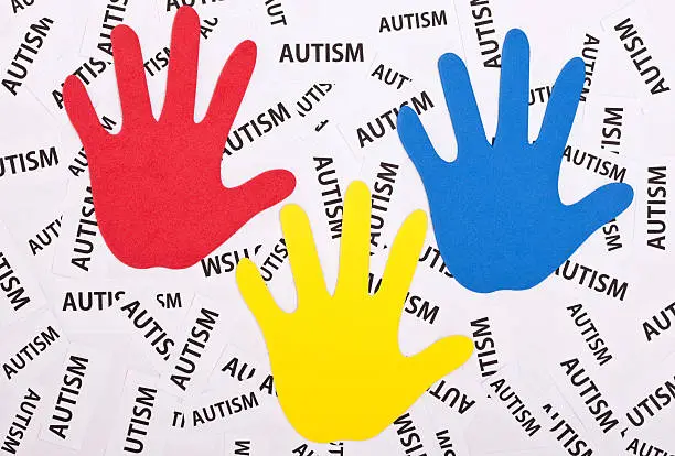 Colorful hand prints with the word autism on many small pieces of paper behind them.