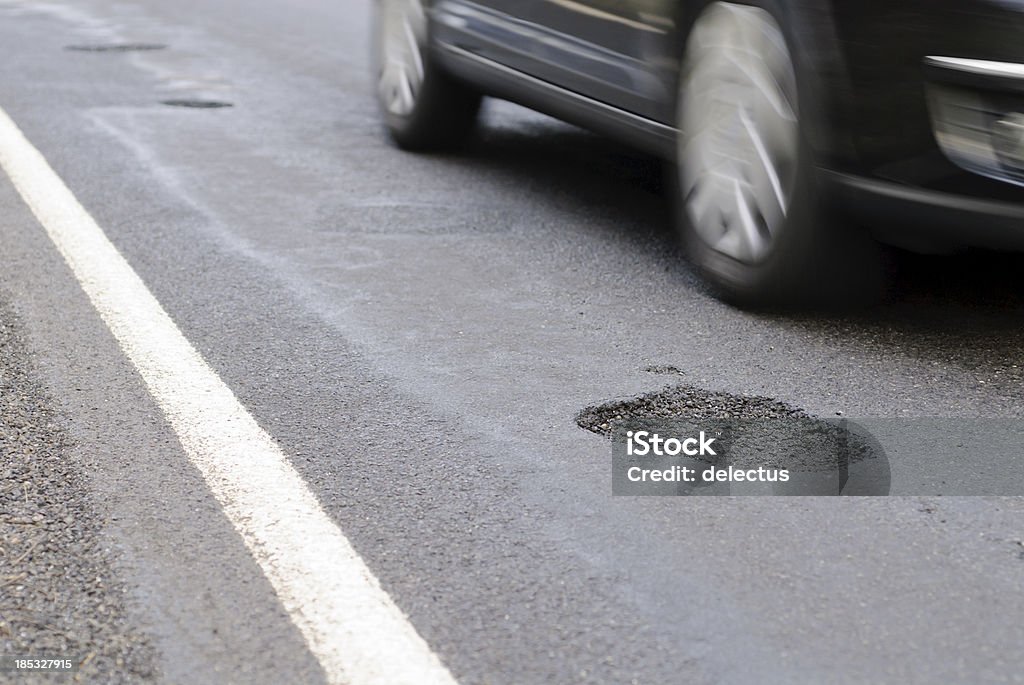 Pothole on the road next to a driving car Car drives past a pothole. Pot Hole Stock Photo