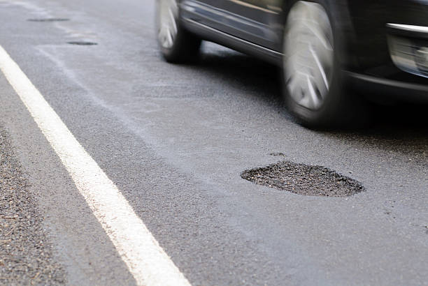 Pothole on the road next to a driving car stock photo