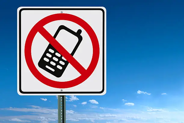 A no cell phone sign post over a blue sky - clipping path included