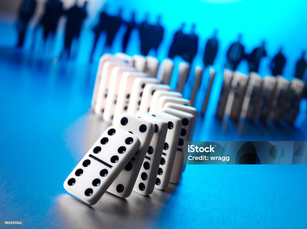 Buisness Team with a Donimo Effect Domino effect on a stainless steel background with blue lighting. A row of business people in the background. Teamwork concept.Click on the link below to see more of my business and sport images. Domino Stock Photo