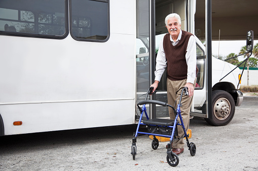 Senior man (60s) with walker walking away from shuttle bus.