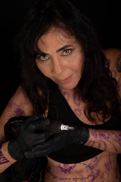 Beautiful artist holding tattoo machine looking at camera against black background