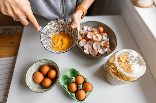 A woman cooks food in the home kitchen. Eggshells waste is placed in a recycling bowl