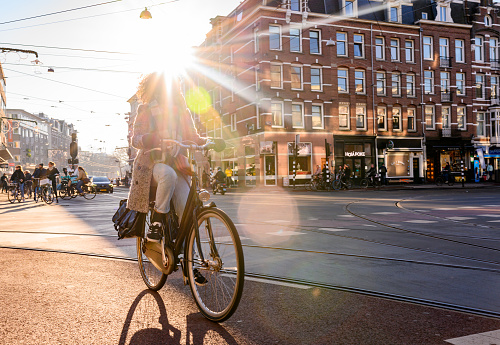 In Amsterdam, Netherlands an unrecognizable woman rides a bike on a city street and is backlit with the sun on a winter morning.
