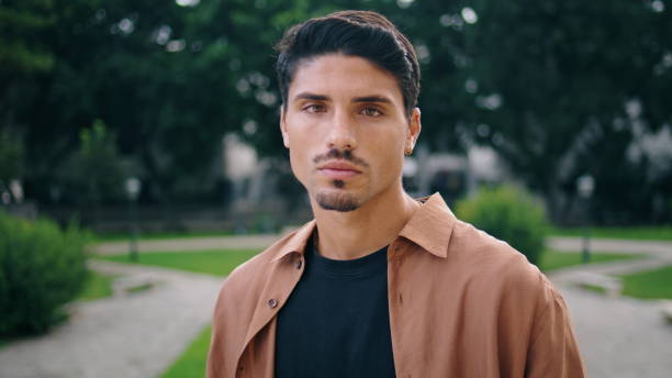 Serious guy posing park portrait. Young man face looking camera standing nature