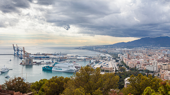 Málaga, Spain - 30th October 2023: Elevated view of partof Málaga, looking down to the Port of Málaga. The Balearia cruiseferry Rusadir and a super-yacht are among the boats in the harbour There are high-rise apartment blocks, with mountains in the background.