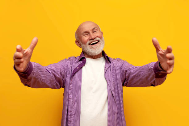 istock old bald grandfather in purple shirt pulls his hands forward and hugs on yellow isolated background, elderly pensioner 1853563185