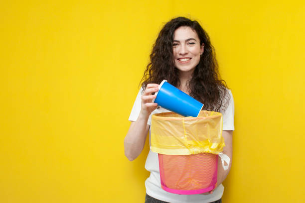 istock young cheerful girl throws plastic glass into a trash can, woman throws out garbage on yellow background 1853566310