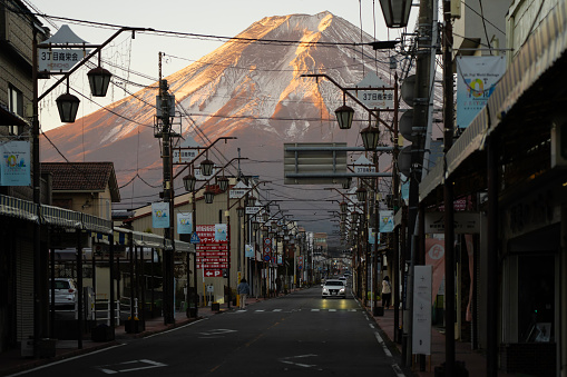 Fujiyoshida, Japan - December 7, 2023: Traffic and shops along Shimoyoshida Honcho Street at dawn, with Mount Fuji seen in the background.