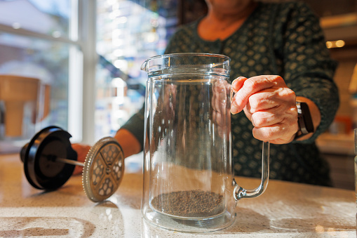 French Press with granulated tea on the table: unrecognizable senior woman hands brewing fresh tea in the kitchen