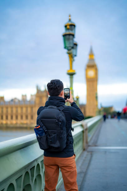 istock Unrecognizable young Latin male in casual clothes with backpack standing on bridge and take photos of Big Ben against clock tower in London with smartphone 1853675585