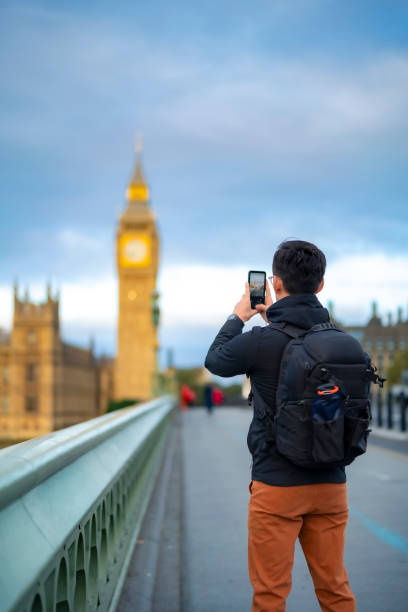 istock Unrecognizable young Latin male in casual clothes with backpack standing on bridge and take photos of Big Ben against clock tower in London with smartphone 1853676126