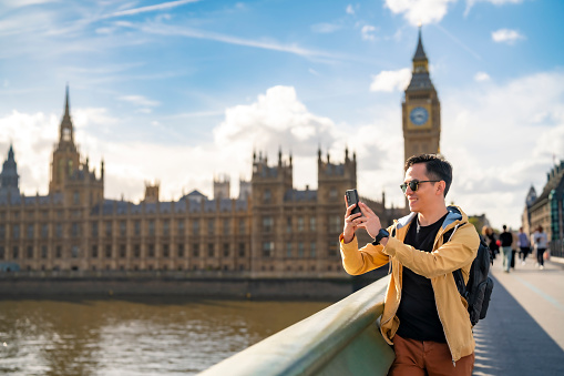 Happy Latin man tourist wearing sunglasses while taking photos with against Big Ben in London