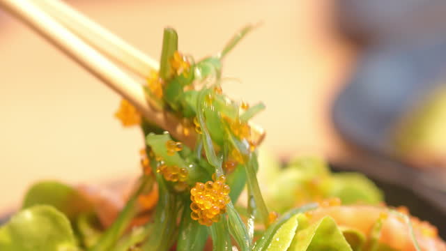 Close up chopsticks pick up seaweed.