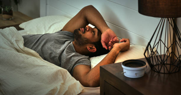 Thinking, depression and asian man in a bed with insomnia, fatigue or sleep paralysis anxiety. Burnout, conflict and male person in a bedroom with overthinking stress, ptsd or mistake trauma in house stock photo