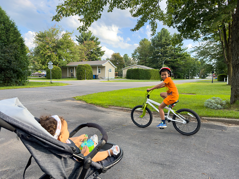 Boy on a bicycle and girl in a stroller walk on the street