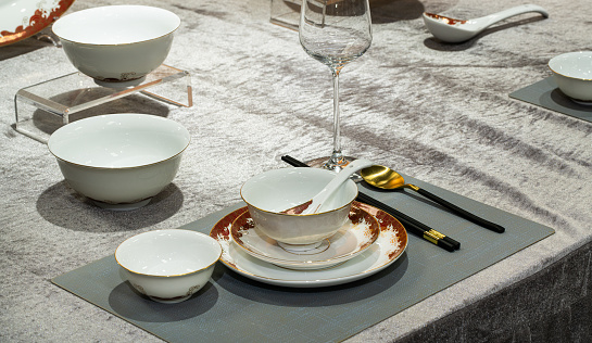 White dishware stacked on a wooden table against white background with transparent wineglasses. Copy space.