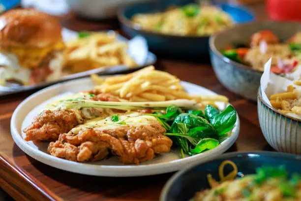 Close-up shot a plate in a restaurant features crispy fried chicken, generously adorned with a tantalizing layer of melted cheese, creating an appetizing and savory dish. Close-up shot a plate in a restaurant features crispy fried chicken, generously adorned with a tantalizing layer of melted cheese, creating an appetizing and savory dish.
