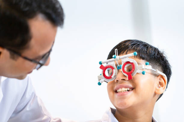 istock Boy doing an eye test checking examination with optometrist in the optical shop, Smiling Indian-thai boy choosing glasses in an optics store 1853909938