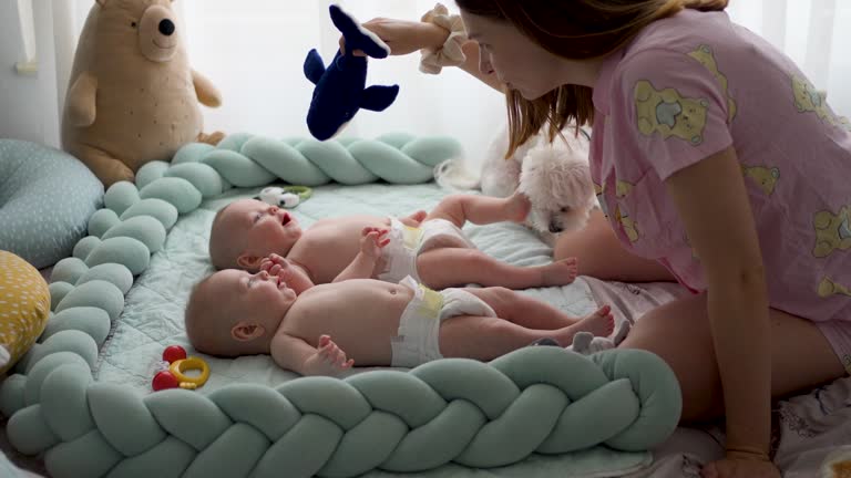 Mother playing with her twin baby boys in the morning in bed