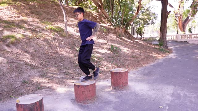 Slow-motion video footage shows a kid demonstrating a squat on a log for knee and thigh muscle training in a public fitness park.