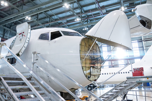 Front view of the white passenger airlines under maintenance in the aviation hangar. The jetliner has opened weather radar. Checking mechanical systems for flight operations