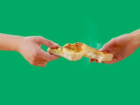 Side view of two people sharing a slice of pide; Turkish bread on a green background