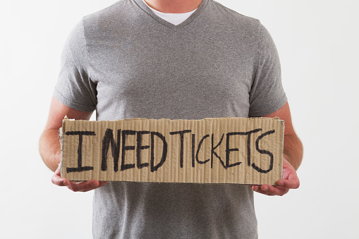 a man holding a sign that says I need tickets. Ticket scalper.