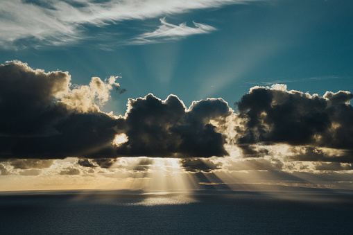 Dramatic view of sunbeams shining over the ocean as the sun rises behind fluffy clouds off the shore of Hawaii. Hope, possibility and motivation concepts.