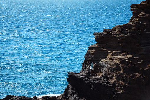 Wide shot of an active and adventurous Indian man hiking a rocky trail overlooking the ocean in Hawaii.