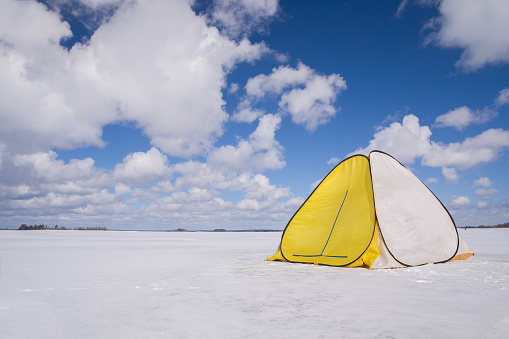 The fishing tent stands on the ice of the lake. Blue sky and clouds.