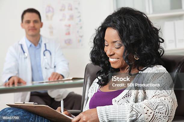 Female Patient Filling Out Forms At Doctors Office Stock Photo - Download Image Now