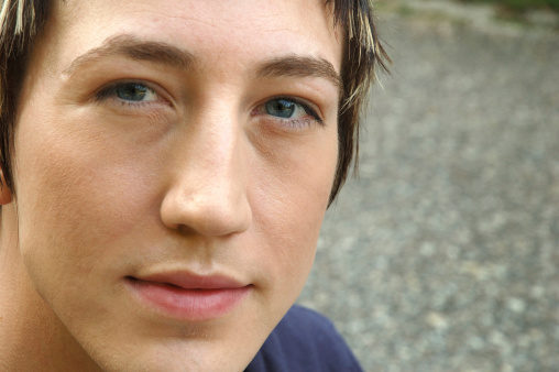 Closely cropped face of young man looking intensely and directly at viewer with an honest expression. Blue eyes. Copyspace.
