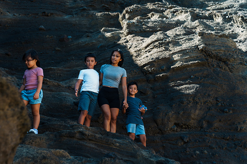 Young and adventurous Asian mother climbing on rocks with her children while at the beach in Hawaii.