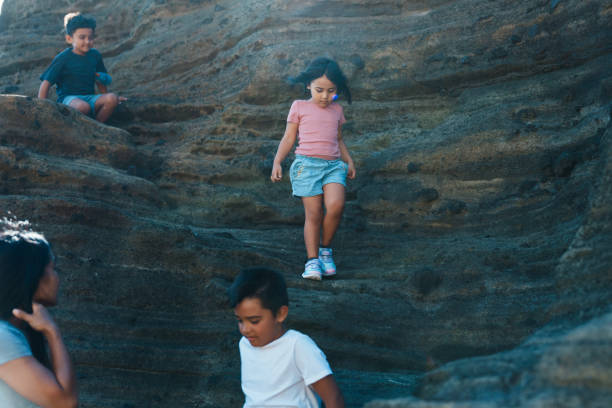 istock Kids having fun scrambling up rocks at the beach with their mom 1854095349