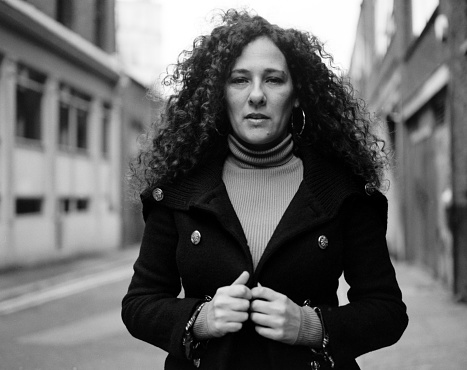 Analog monochrome portrait of mature woman in London street. Her hair is curly and she is wearing a thick winter coat. Confident and proud expression.