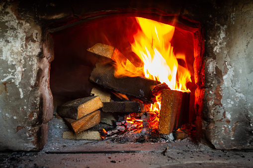 A stack of wooden planks is burning in an old stone hearth. Smoke and fire go up the chimney.