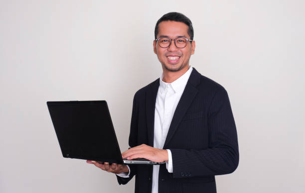 istock Asian businessman smiling confident while holding a laptop 1854132293