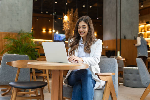 istock Young woman, digital nomad working remotely from a cafe, drinking coffee and using laptop, smiling. 1854145425