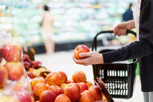 Asian beautiful young woman shopping a fruits and vegetables in local grocery store, woman picking up a fruits from shelf and put it into the fabric reusable bag. Sustainable lifestyles concept.