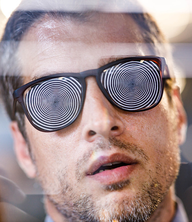 Close up of controlled man with hypnotic eyeglasses who is unable to see the true reality. The view is through glass.