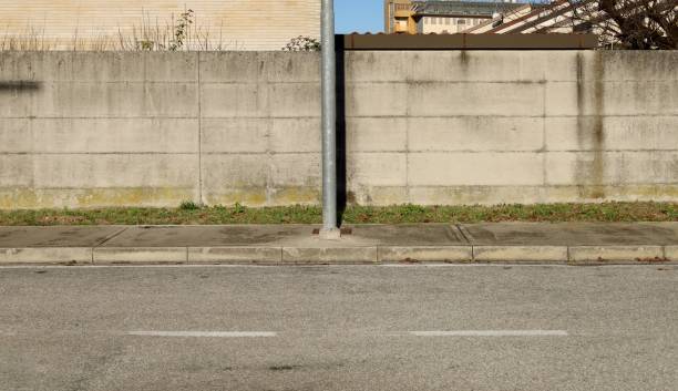 istock Metallic pole on cement sidewalk with precast concrete wall, a brick wall and residential buildings on behind. Urban street in front. 1854192078