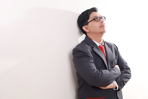 Stressed sad asian businessman leaning on the wall while thinking something. Isolated on white background with copyspace