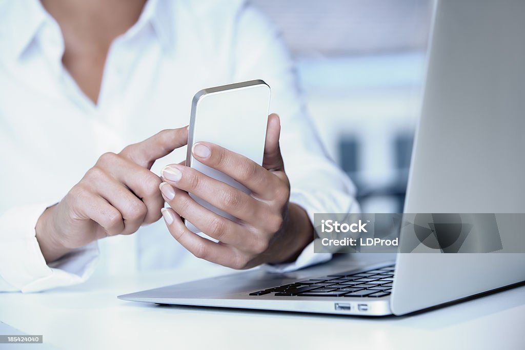 Hands holding cell phone with laptop nearby close-up woman laptop mobile phone finger button enter desk Adult Stock Photo