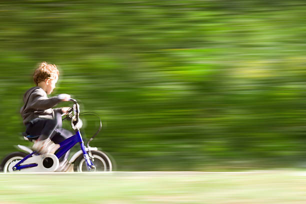 Young boy riding a bicycle on a forest track, without helmet, blurred motion.