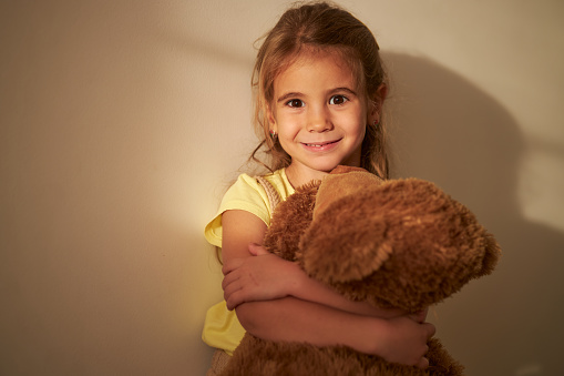 Cute little girl embracing her teddy bear indoors
